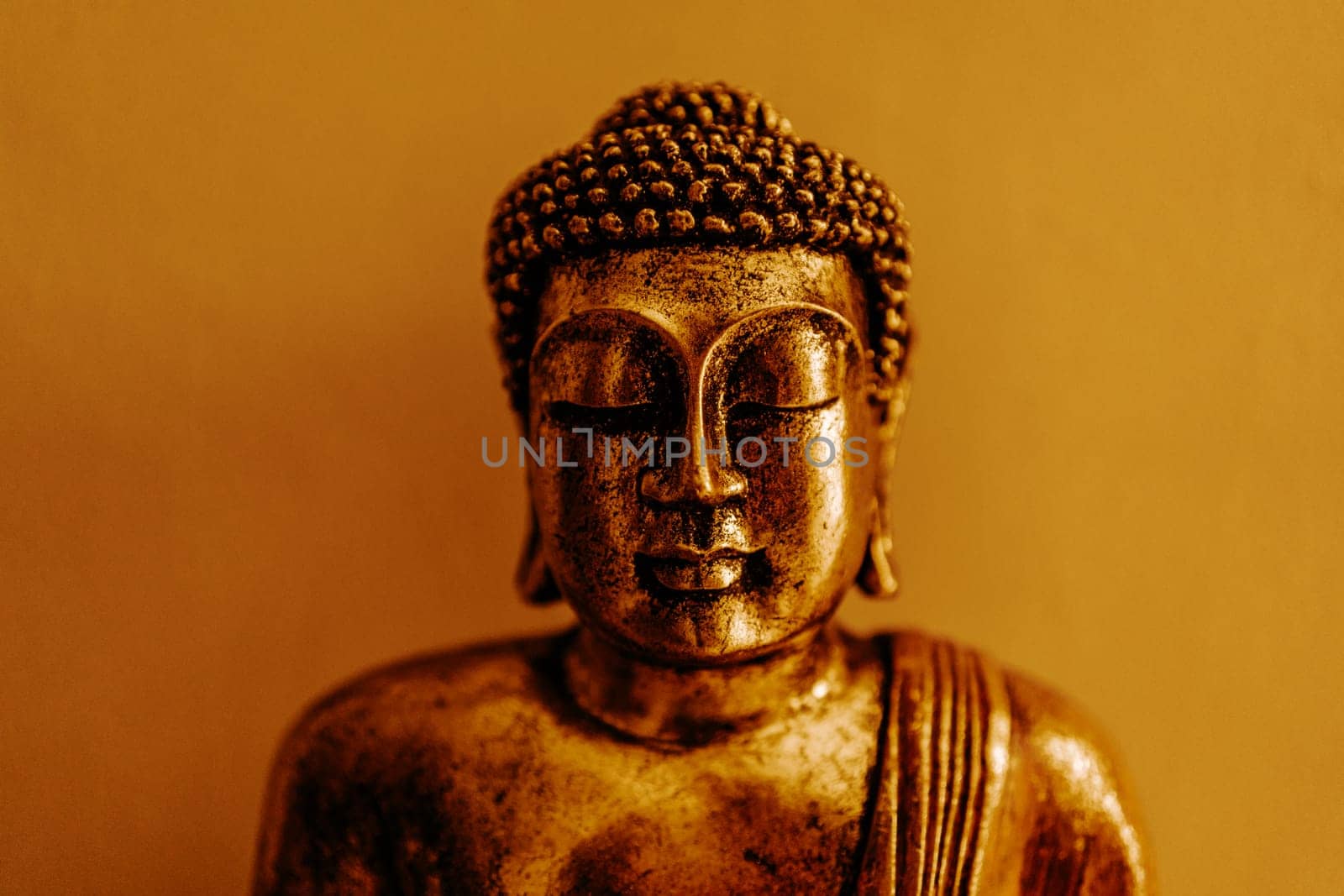 Golden buddha statue portrait in sitting meditation pose on wall background. Buddhism religion symbol of wisdom and purity