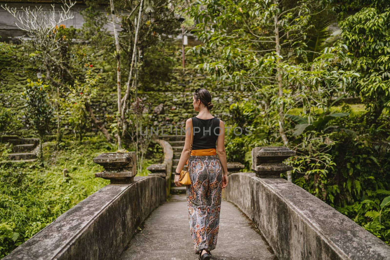 Young stylish girl walking on Pura Gunung Kawi temple bridge. Ancient rocky monument attraction, holy balian royal tombs