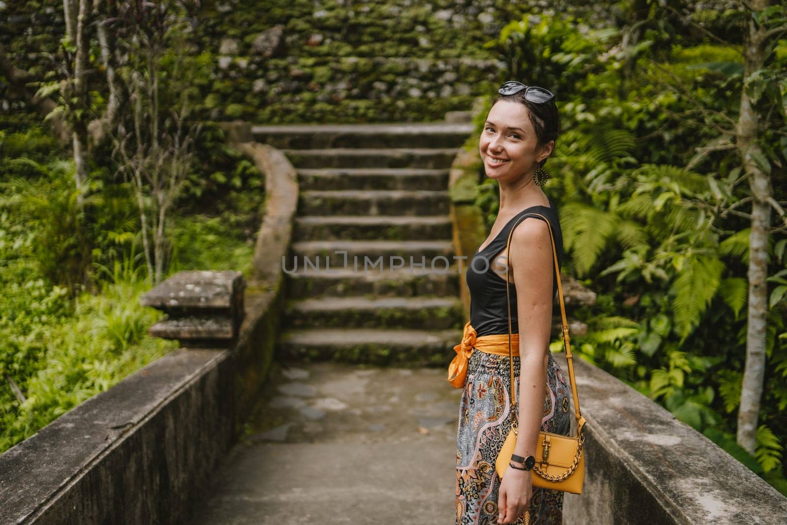 Young stylish girl walking on Pura Gunung Kawi temple bridge. Ancient rocky monument attraction, holy balian royal tombs