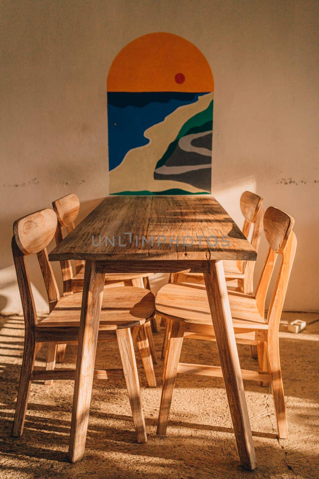 Outdoor summer table in tropical garden. Wooden table with chairs at white wall with decorative painting.