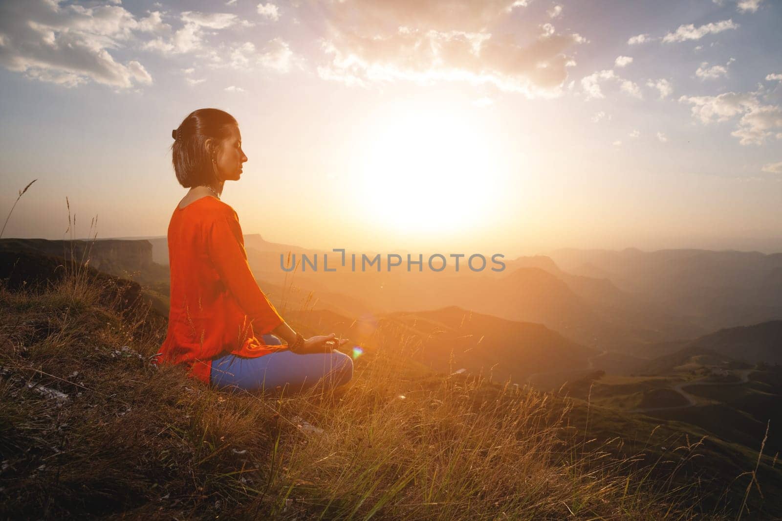 woman practices yoga and meditates on a mountain. Side view of a yogi practicing in the mountains at dawn in the rays of the sun receiving the energy of a new day by yanik88