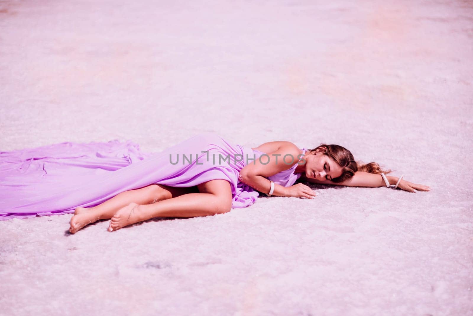 A woman in a pink dress lies on the shore of a pink lake, takes a photo for memory and leaves unforgettable memories