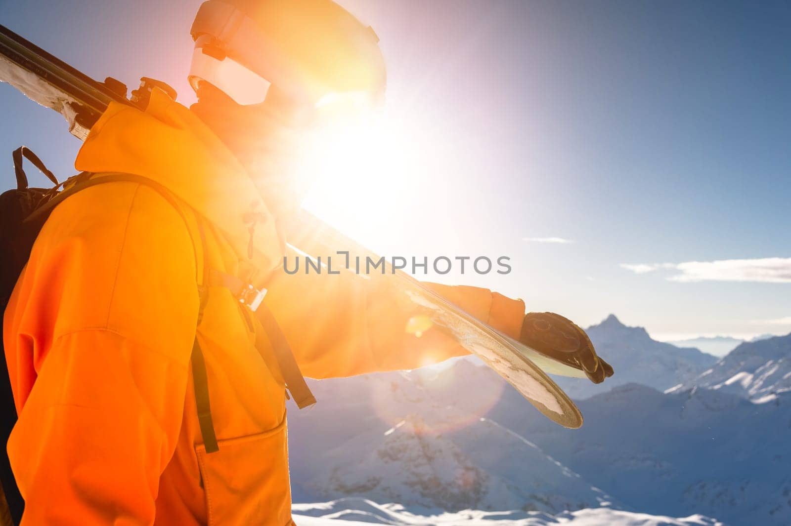 A young skier in ski goggles in the mountains and bright clothes stands against the background of a clear sky and a sunny day. horizontal view.