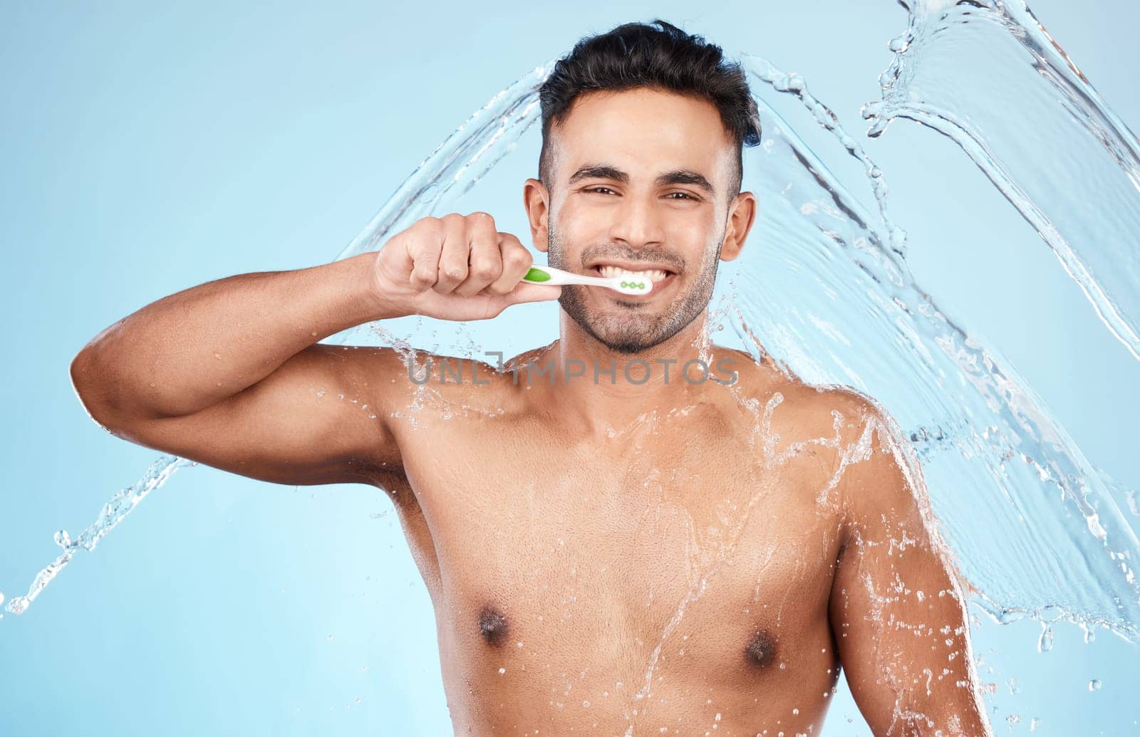 Face, water splash and man with toothbrush for cleaning in studio on blue background. Dental veneers, hygiene and portrait of happy male model brushing teeth for oral wellness, health or fresh breath by YuriArcurs