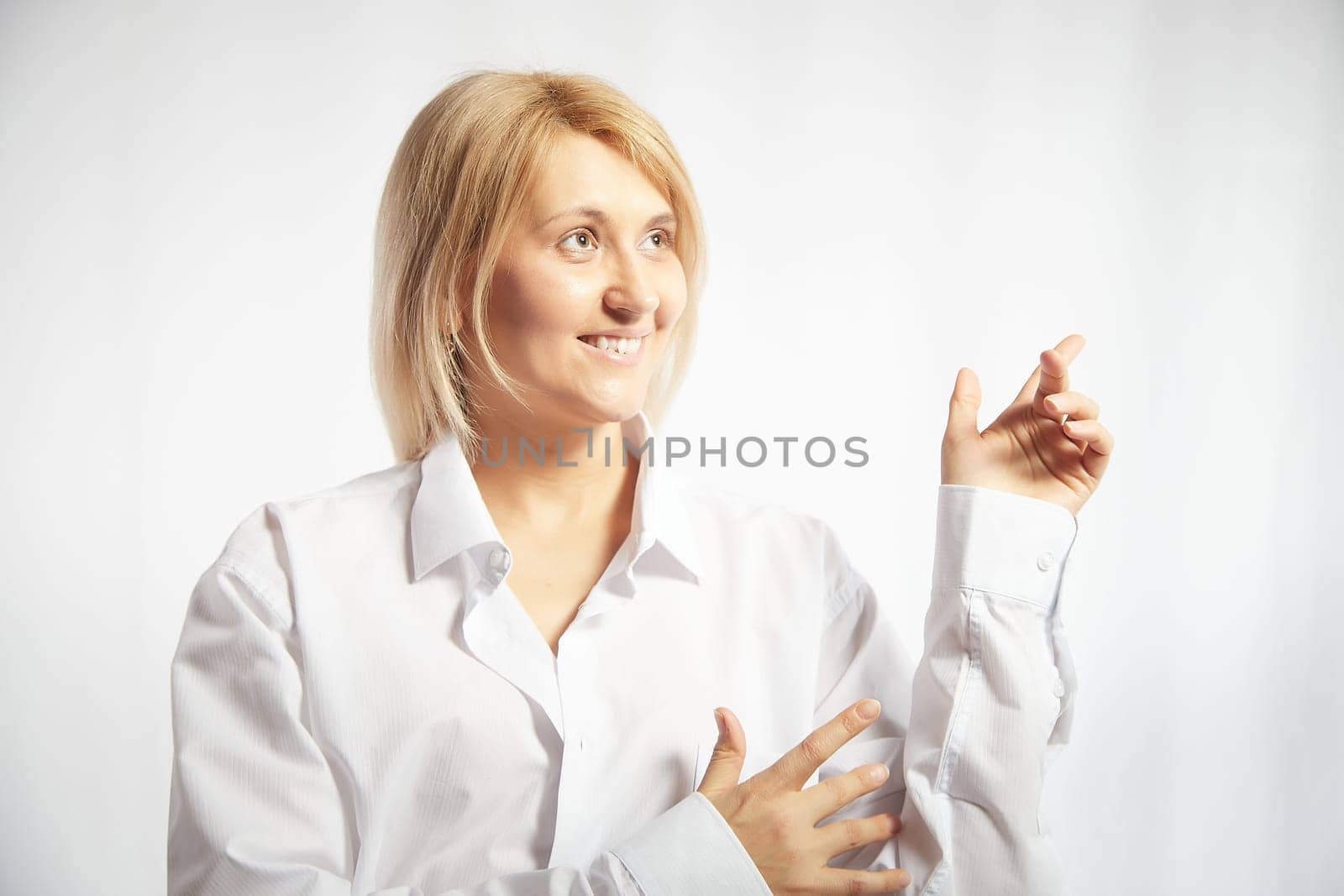 Portrait of a pretty blonde smiling woman posing on a white background and pointing somewhere. Happy girl model in white shirt in studio. Copy space by keleny