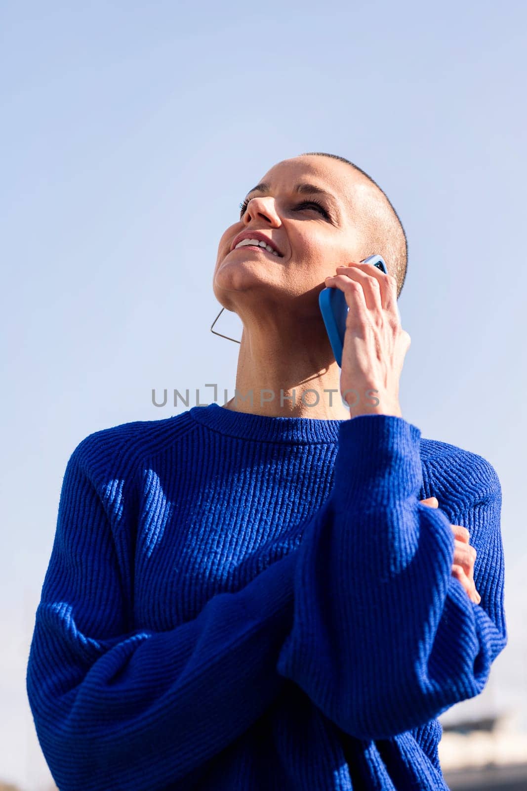 confident woman in blue sweater talking on mobile phone at city, concept or modern lifestyle and technology of communication, copy space for text