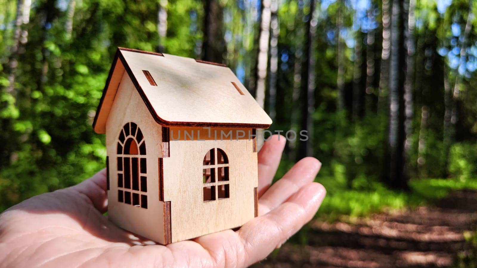 Small wooden toy house on palm of woman hand on natural background. symbol and concept of care of family and buying, selling, donating of eco friendly home. copy space. close-up, soft selective focus by keleny