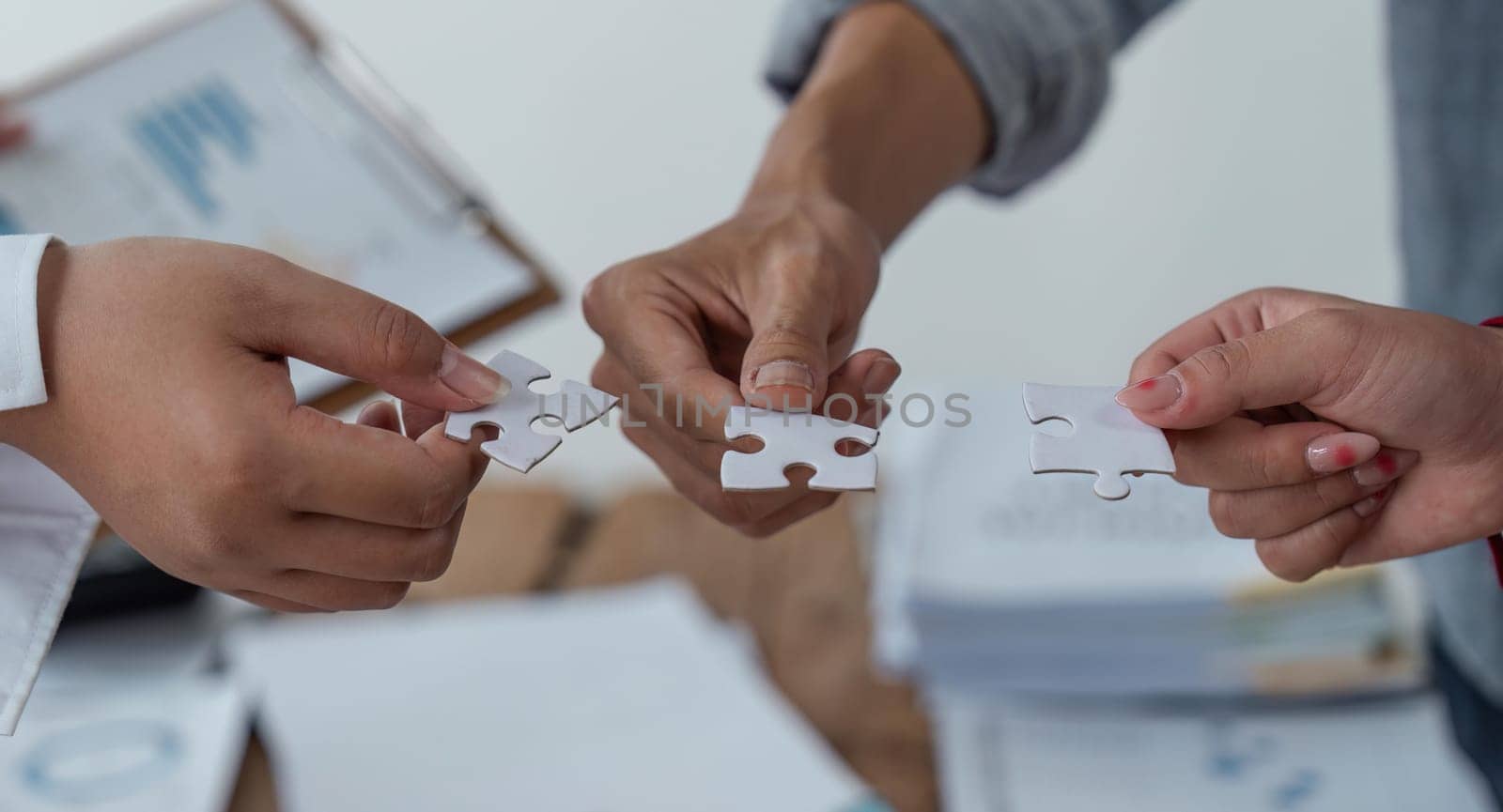 Concept of teamwork and partnership. Hands join puzzle pieces in the office. business people putting the jigsaws team together. Charity, volunteer. Unity, team business by nateemee