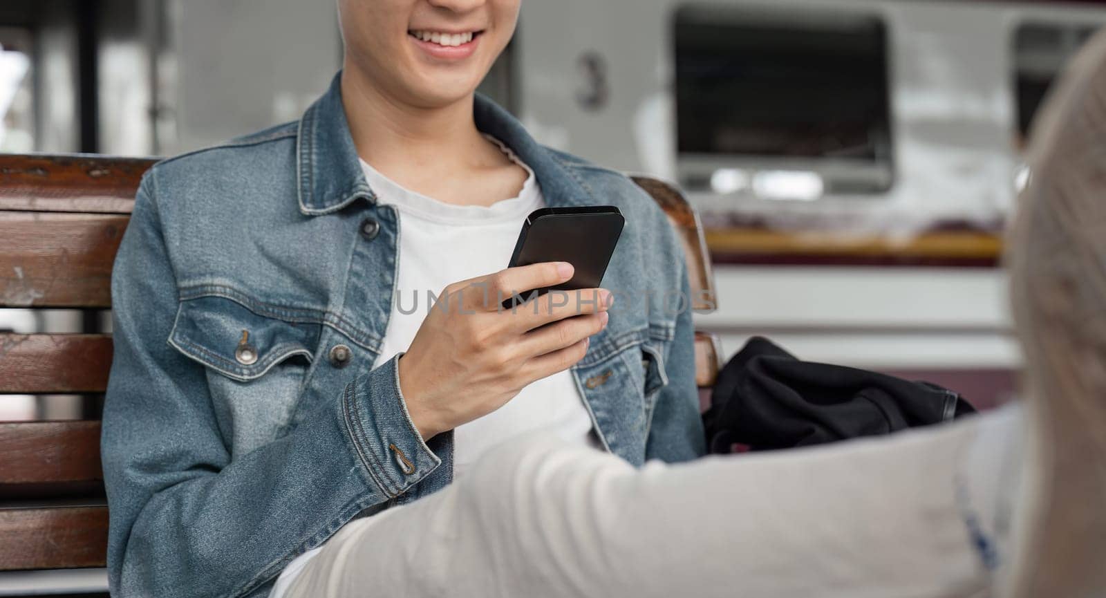 Traveler young asian man using cellphone booking trip at train station. Happy tourist travel by train using smartphone searching location. Male Backpacker arrival at platform railway.