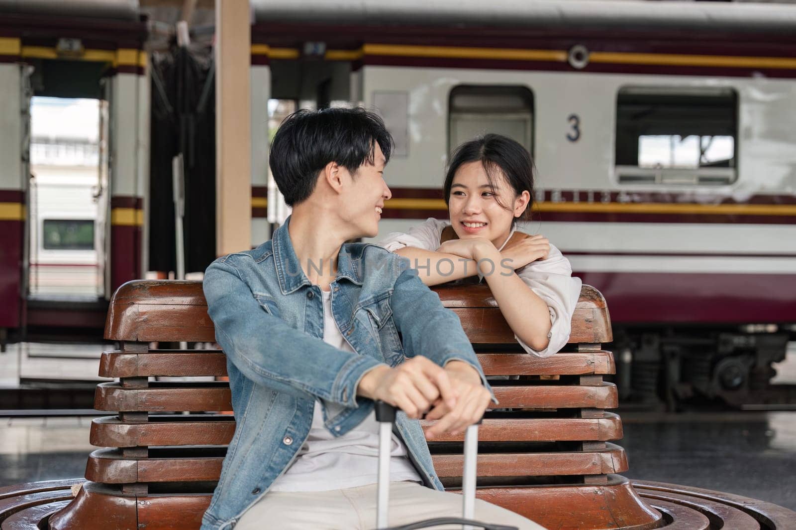 Young couple sitting on wooden bench at train station. Couple sitting waiting for the train at platform by nateemee