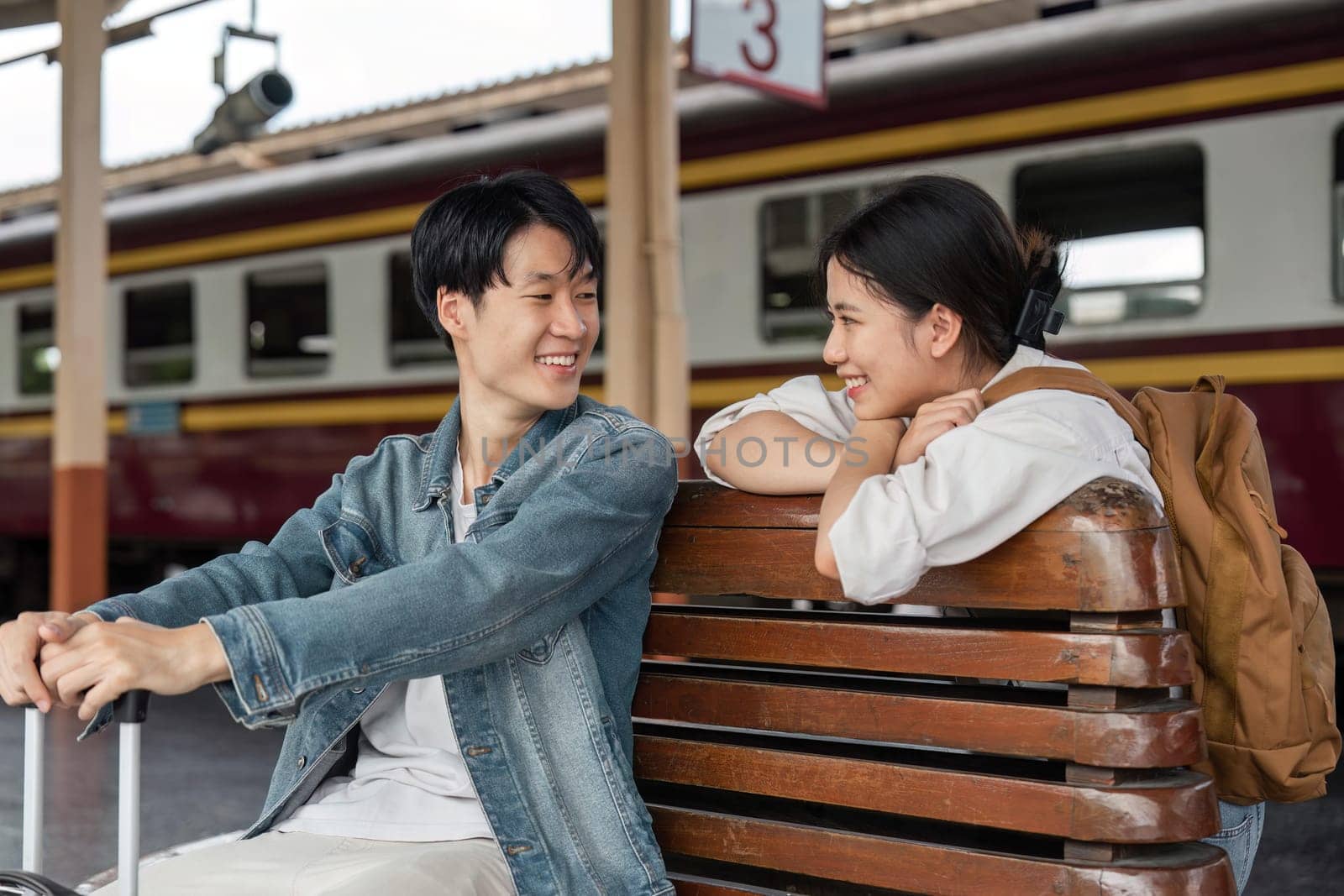 Young couple sitting on wooden bench at train station. Couple sitting waiting for the train at platform.