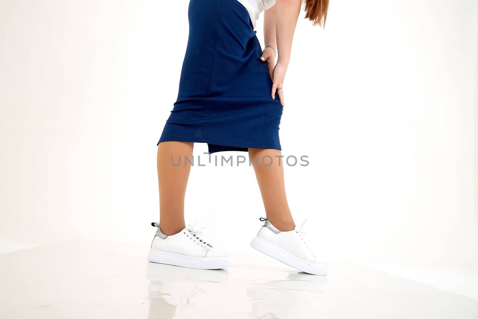 Beautiful white sneakers and woman legs in the studio on white background. Fashionable shooting of young girl with beautiful legs