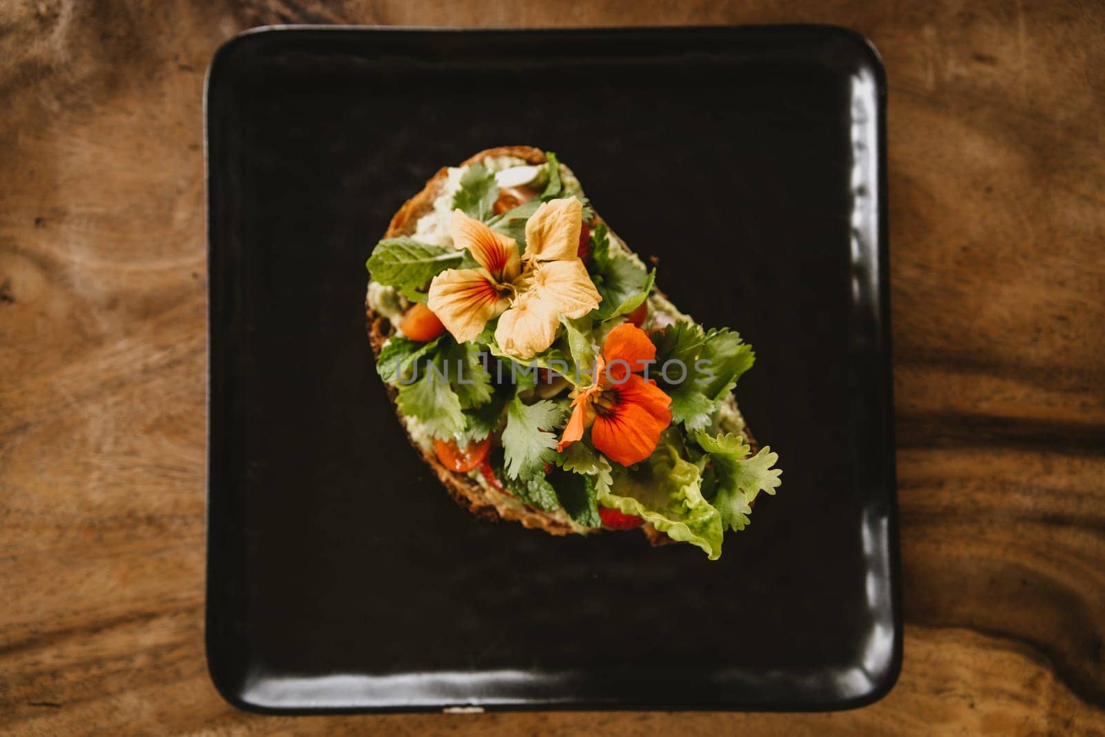 Close up shot of avocado bruschetta with tomatoes and herbs. Morning tropical breakfast toast on black plate