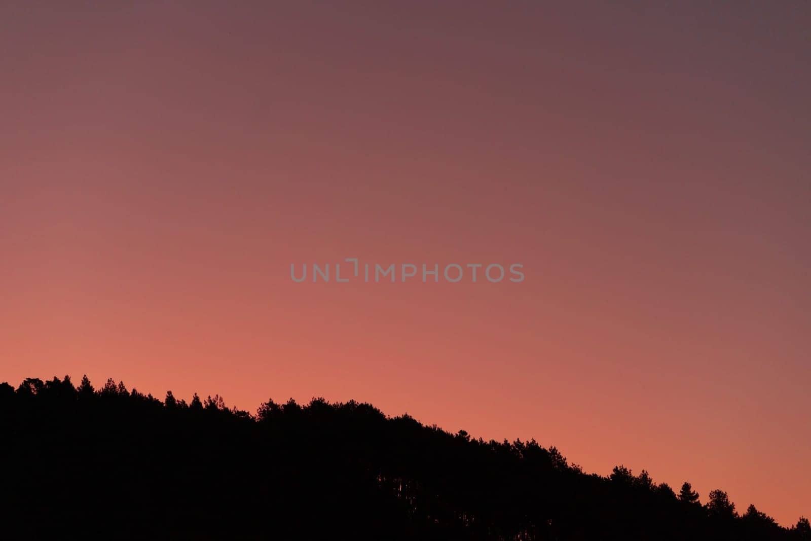 Dark silhouette of hills on pink sunrise view. Sundown landscape with purple color sky