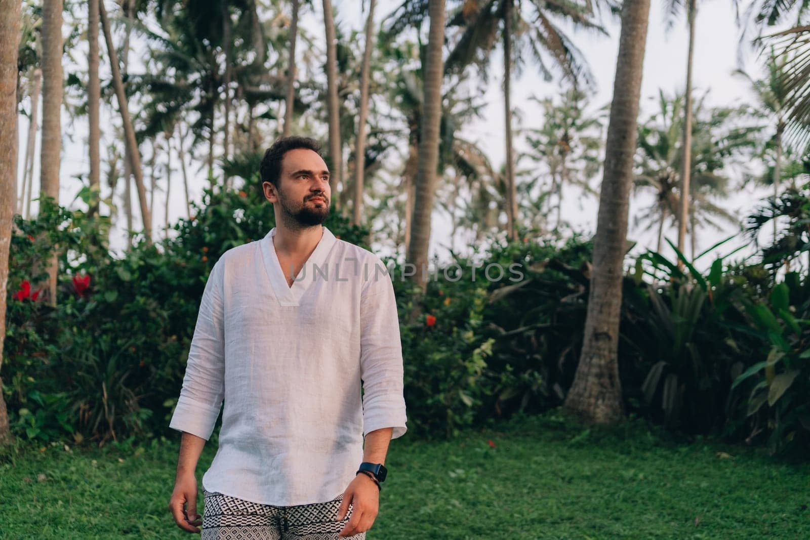 Close up shot of young bearded man in white shirt on green palms background by Popov