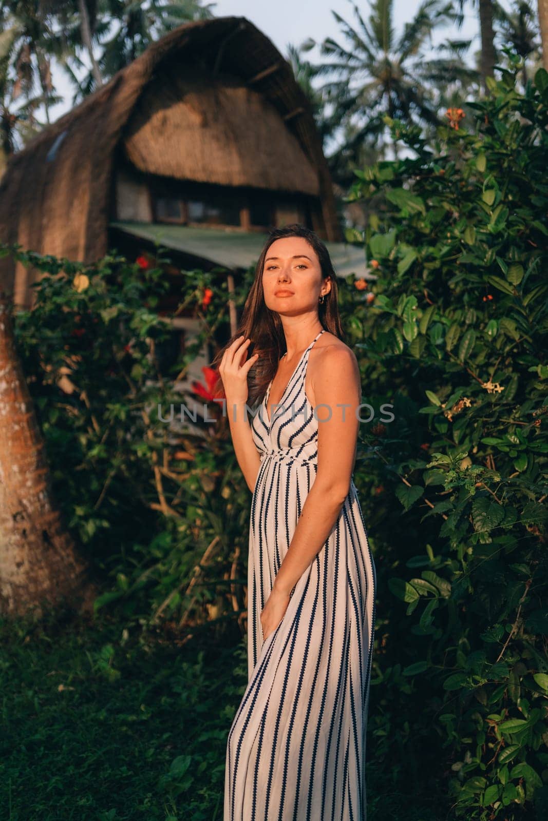 Portrait of beautiful lady in white striped dress with balinese vila background. Young model girl posing in tropical jungle nature