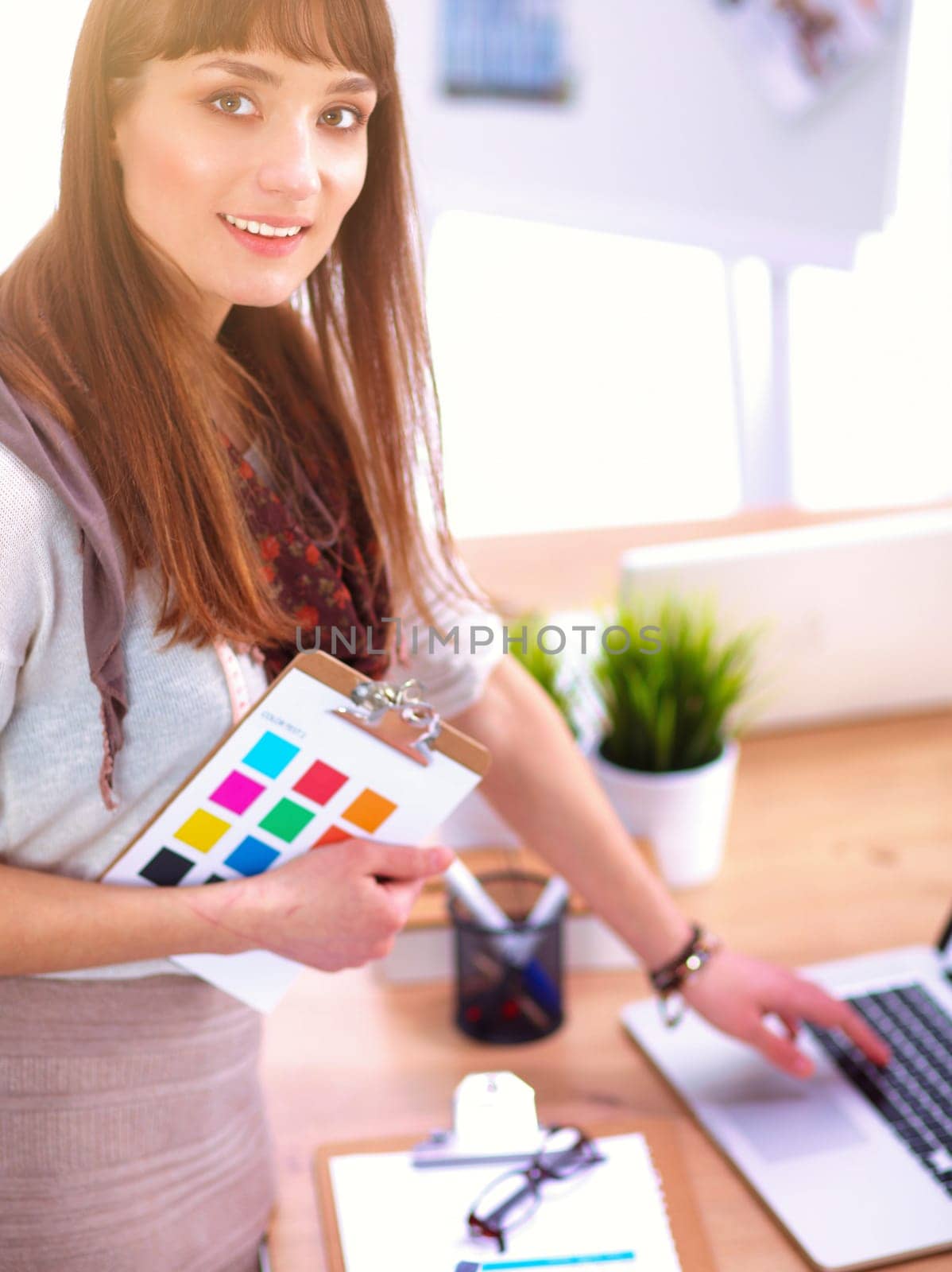 Young attractive fashion designer standing by desk in office, holding folders.