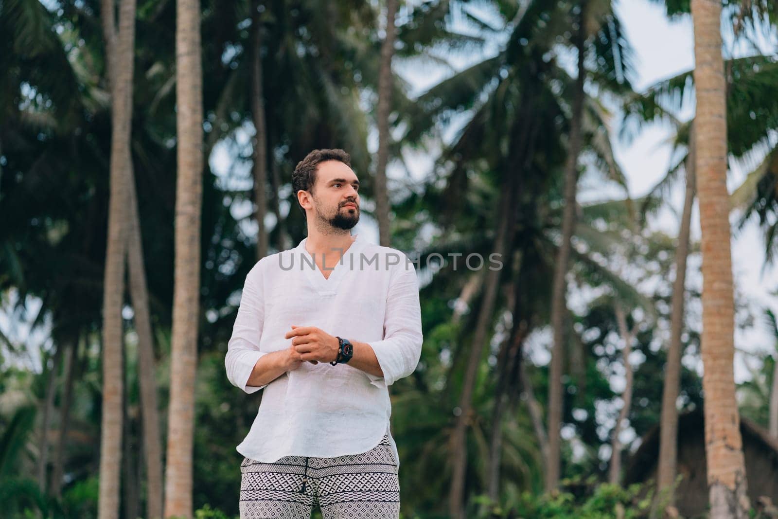 Close up shot of young bearded man in white shirt on green palms background. Male tourist in tropical jungle