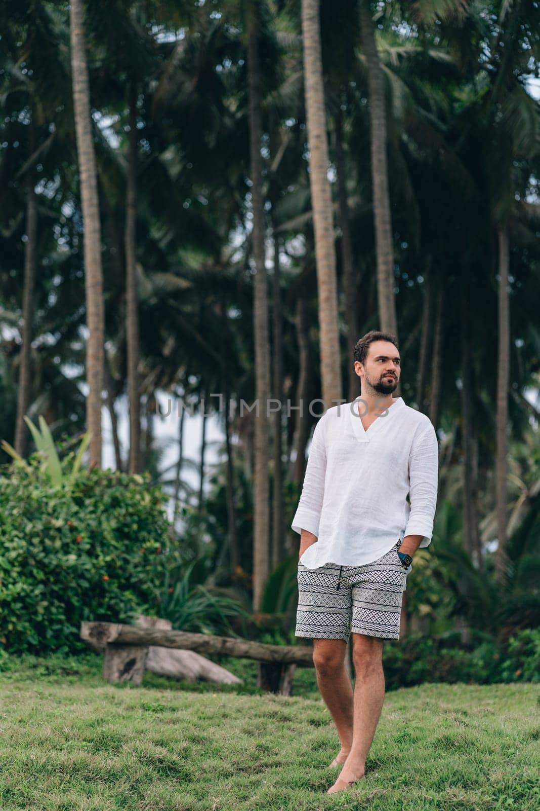 Portrait of casual dressed young man with jungle palms background. Guy in white shirt and shorts enjoy tropical nature environment
