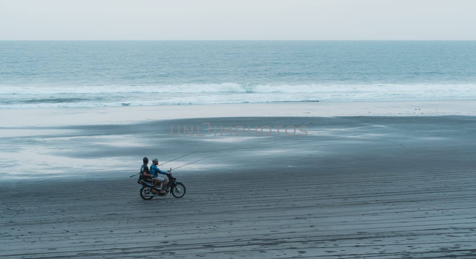 Landscape view of two bikers driving on beach with sea background. Riding a scooter on the ocean sand