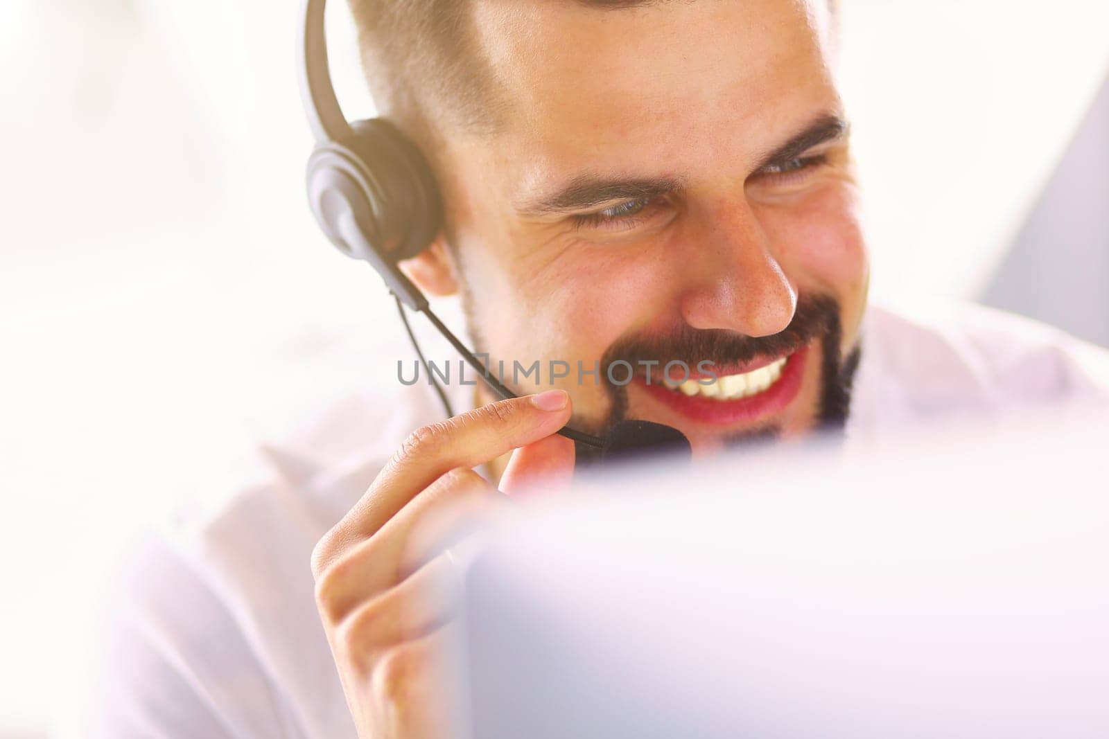 Portrait of a young man with a headset in front of a laptop computer.