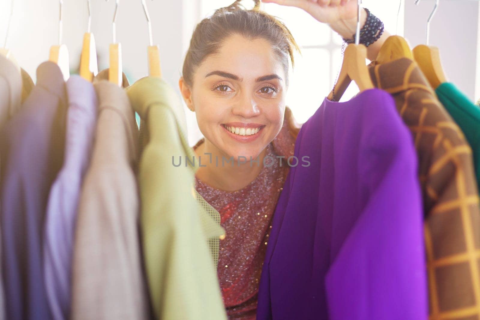 Beautiful young stylist near rack with hangers.