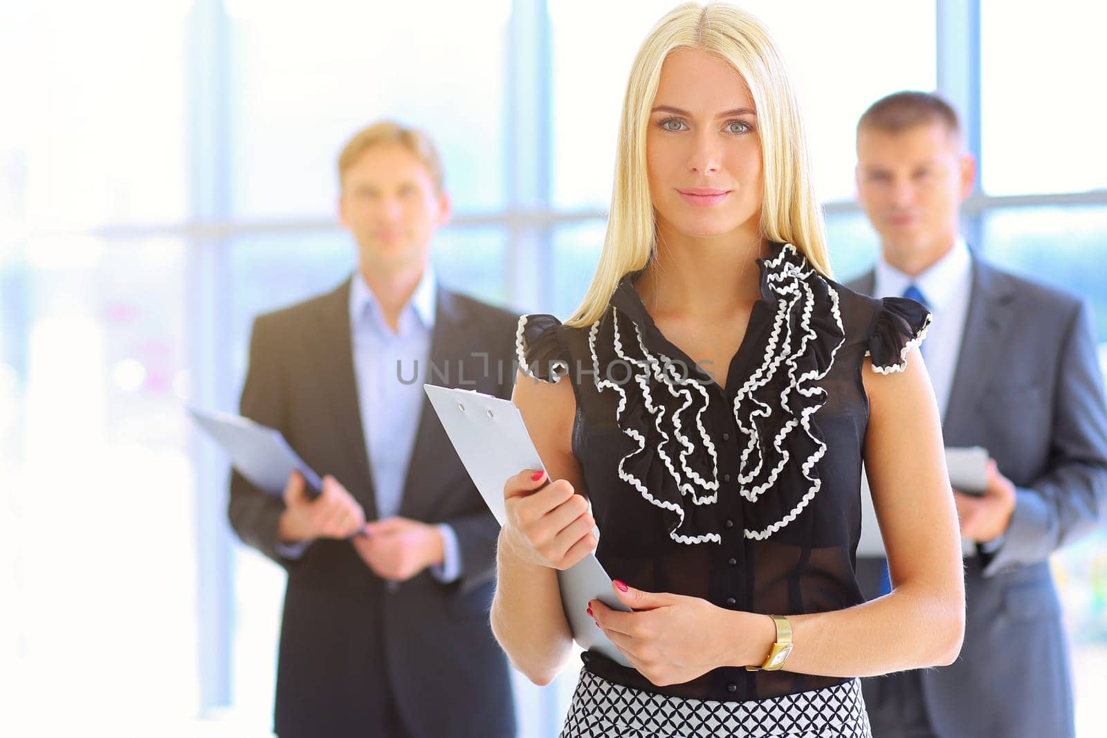 Business woman standing in foreground with a folder in her hands .