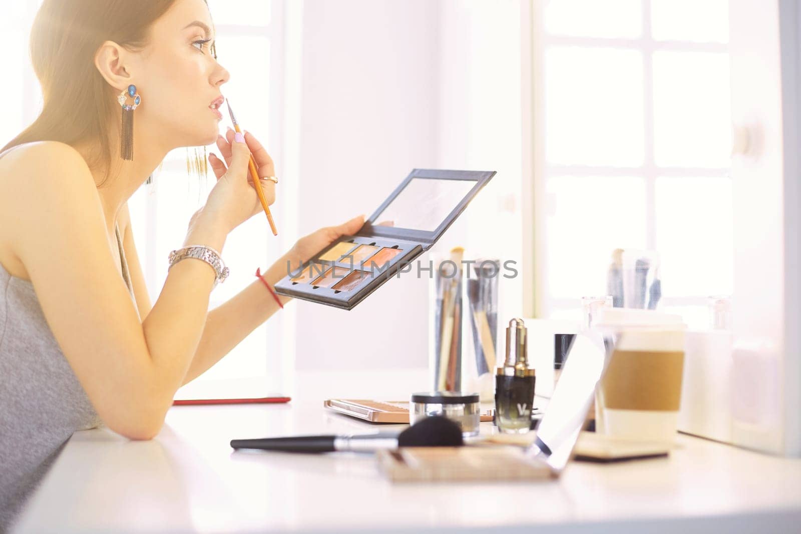 A beautiful young woman sitting at a makeup table and doing her makeup.