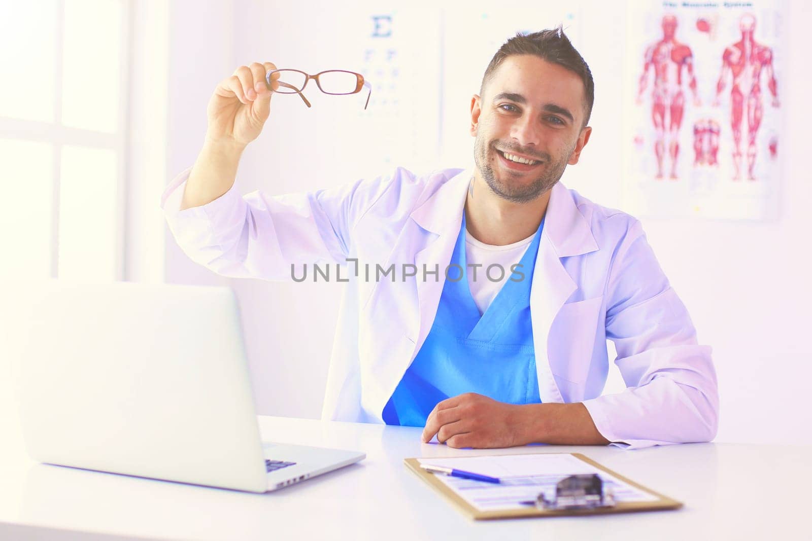 Portrait of a male doctor with laptop sitting at desk in medical office