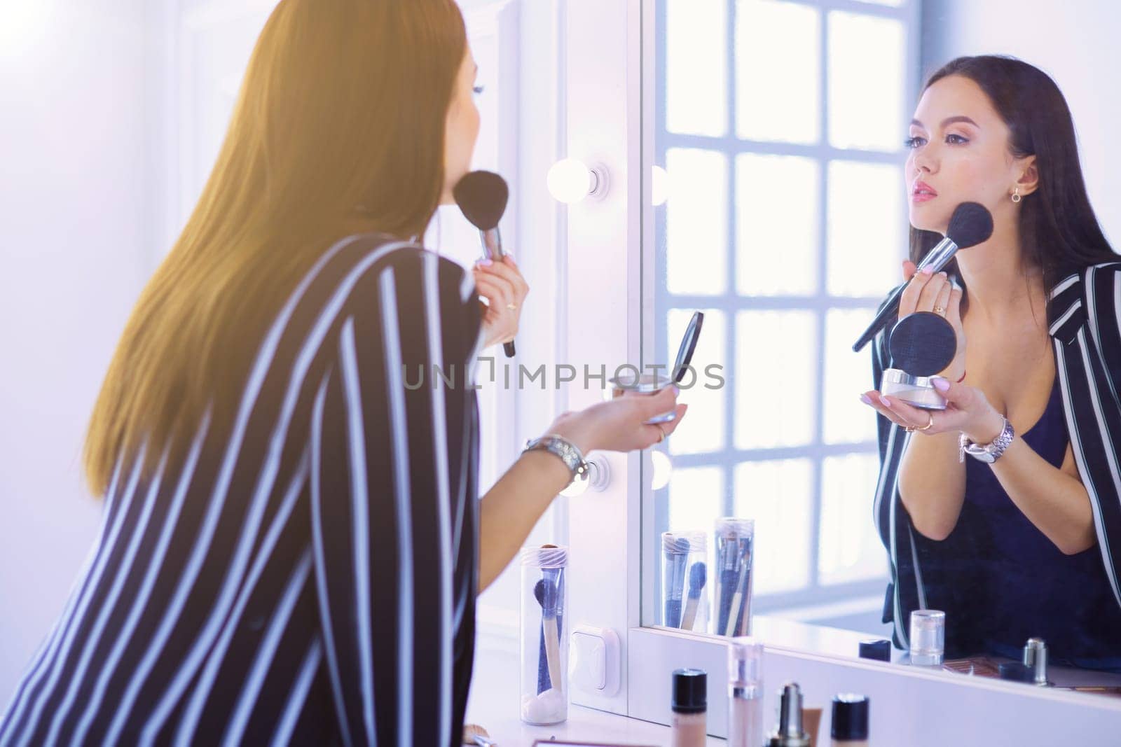 Beautiful girl looking in the mirror and applying cosmetic with a big brush.