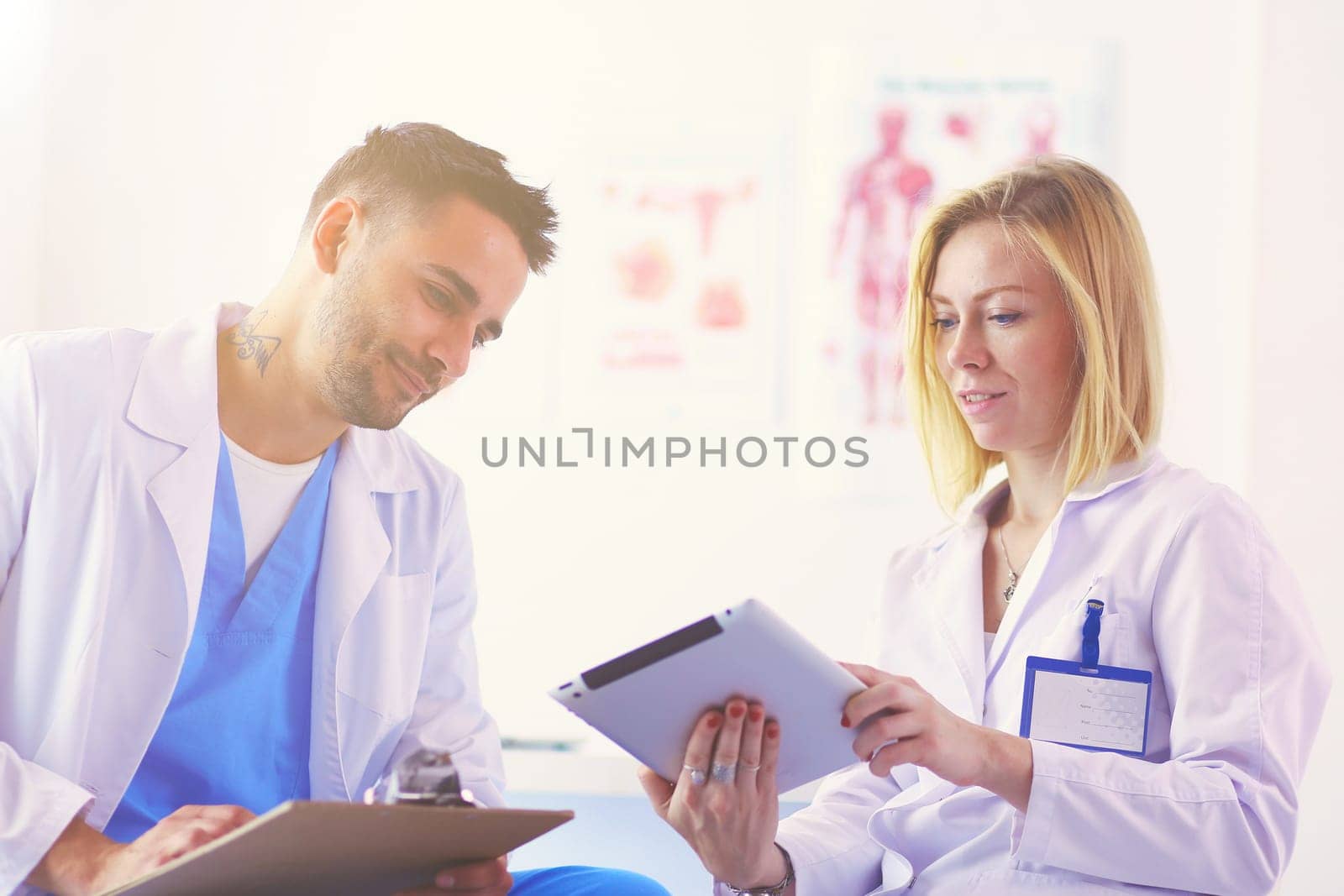 Handsome doctor is talking with young female doctor and making notes while sitting in his office