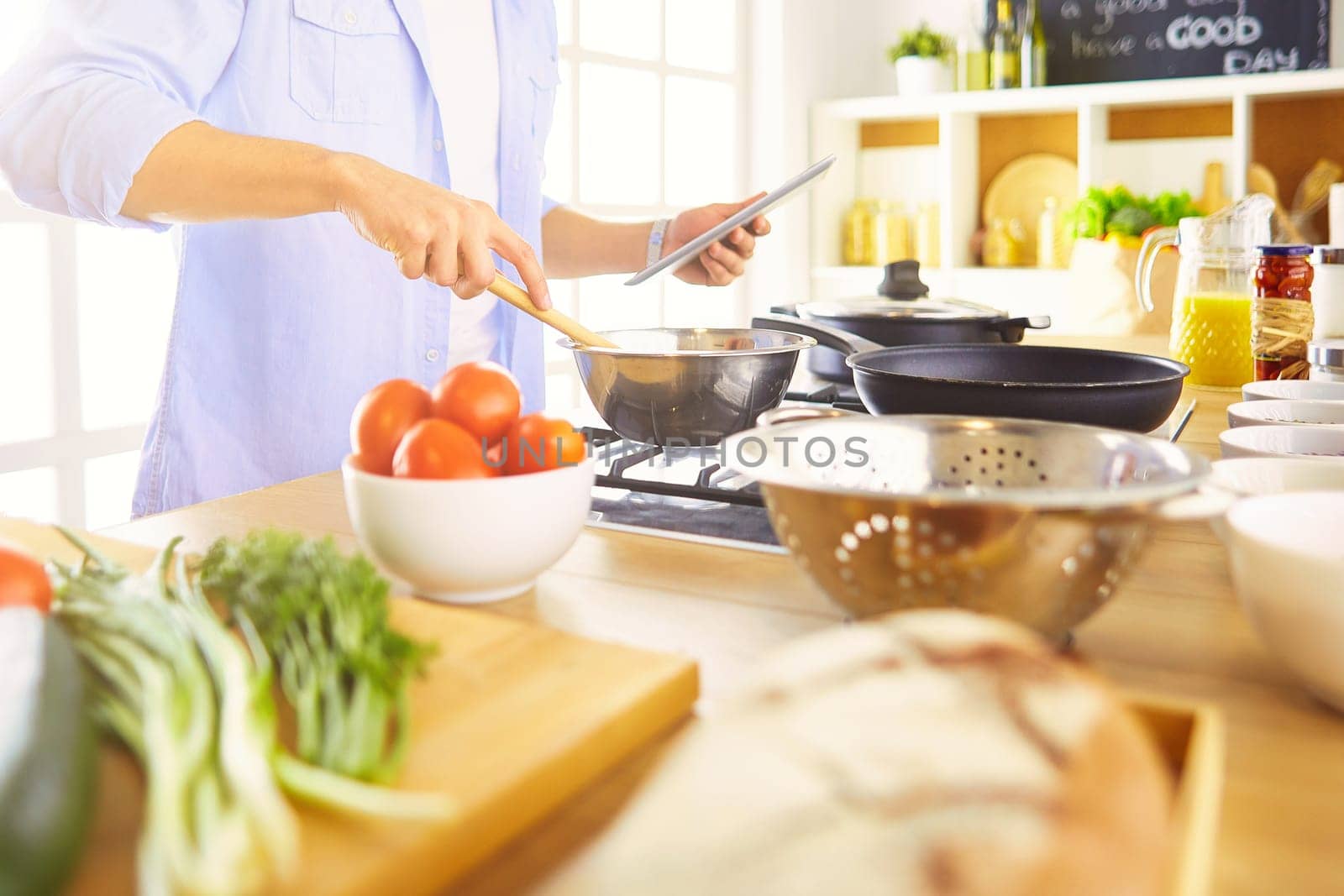 Man following recipe on digital tablet and cooking tasty and healthy food in kitchen at home.