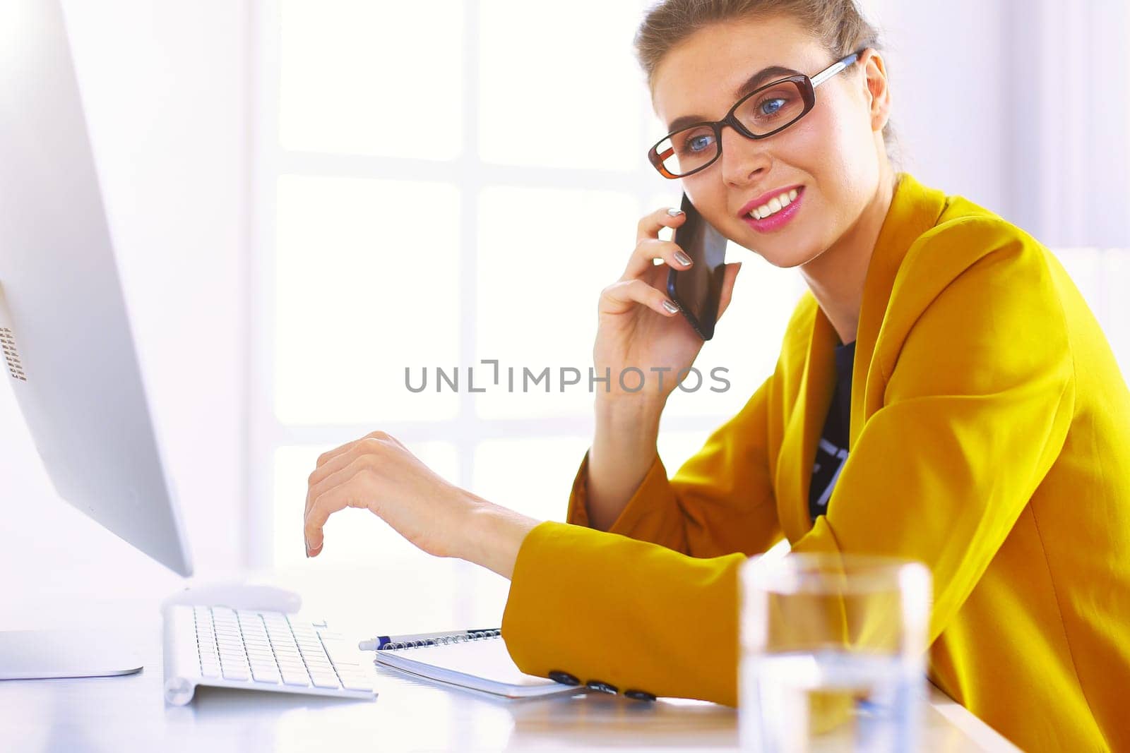 Businesswoman concentrating on work, using computer and cellphone in office.