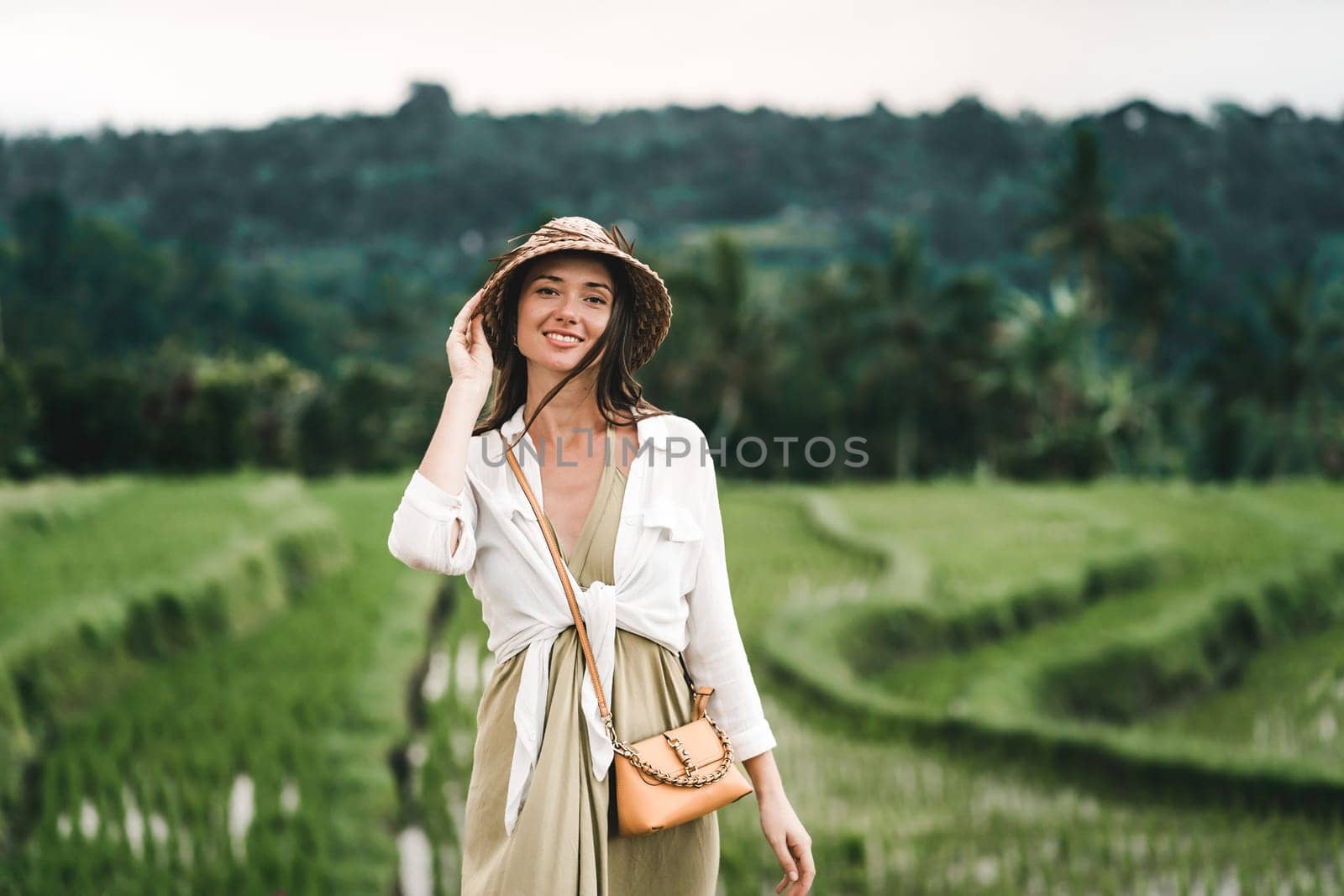 Close up shot of beautiful girl with traditional balinese hat on rice terrace background. Smiling lady in paddy field