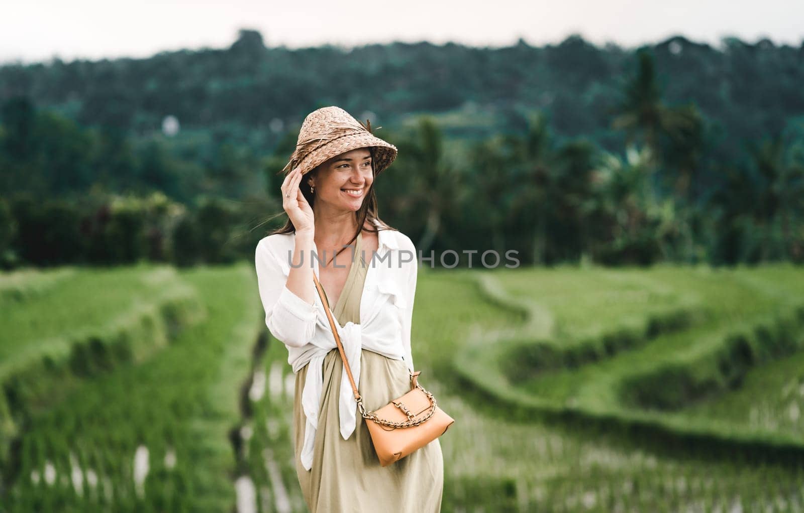 Portrait of happy girl with balinese hat on rice terrace. Excited girl looking around balinese rice plantation