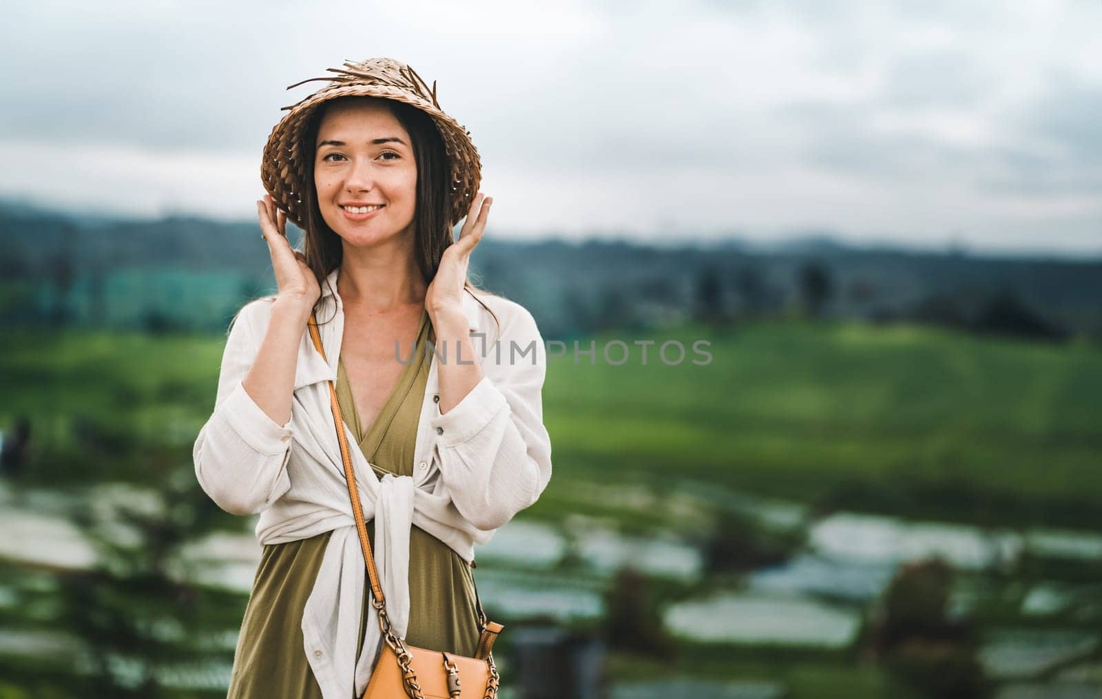 Close up shot of beautiful girl with traditional balinese hat on rice terrace background. Smiling lady in paddy field