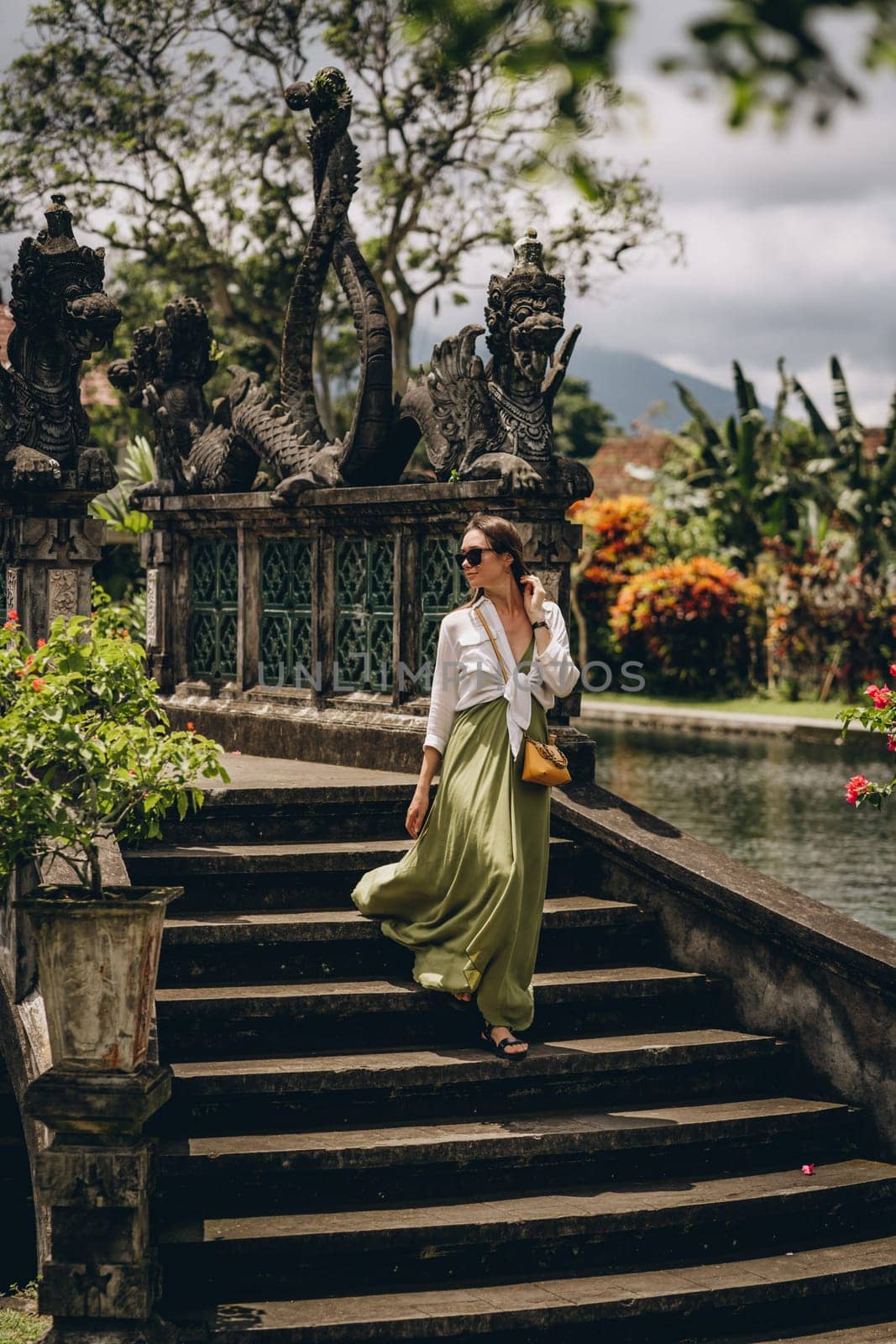 Beautiful girl goes down the stairs in Saraswati lush garden. Lady on traditional balinese stone bridge