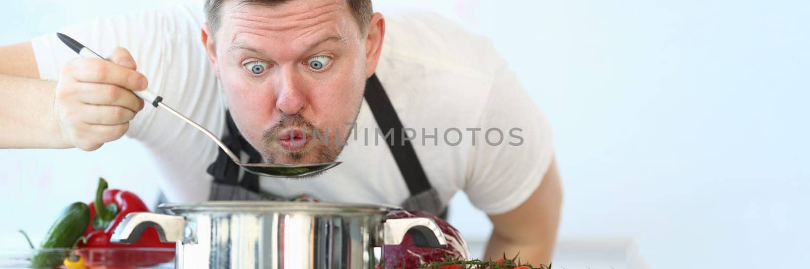 Portrait of male chef preparing and tasting hot food in vegetable soup spoon. Cooking rules and taste qualities of vegetarian food