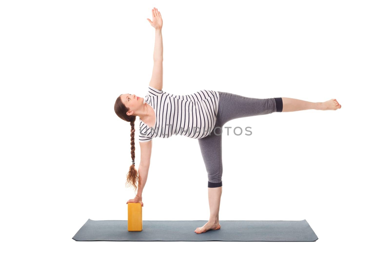 Pregnancy yoga exercise - pregnant woman doing asana virabhadrasana 3 - warrior pose variation with wooden block isolated on white background