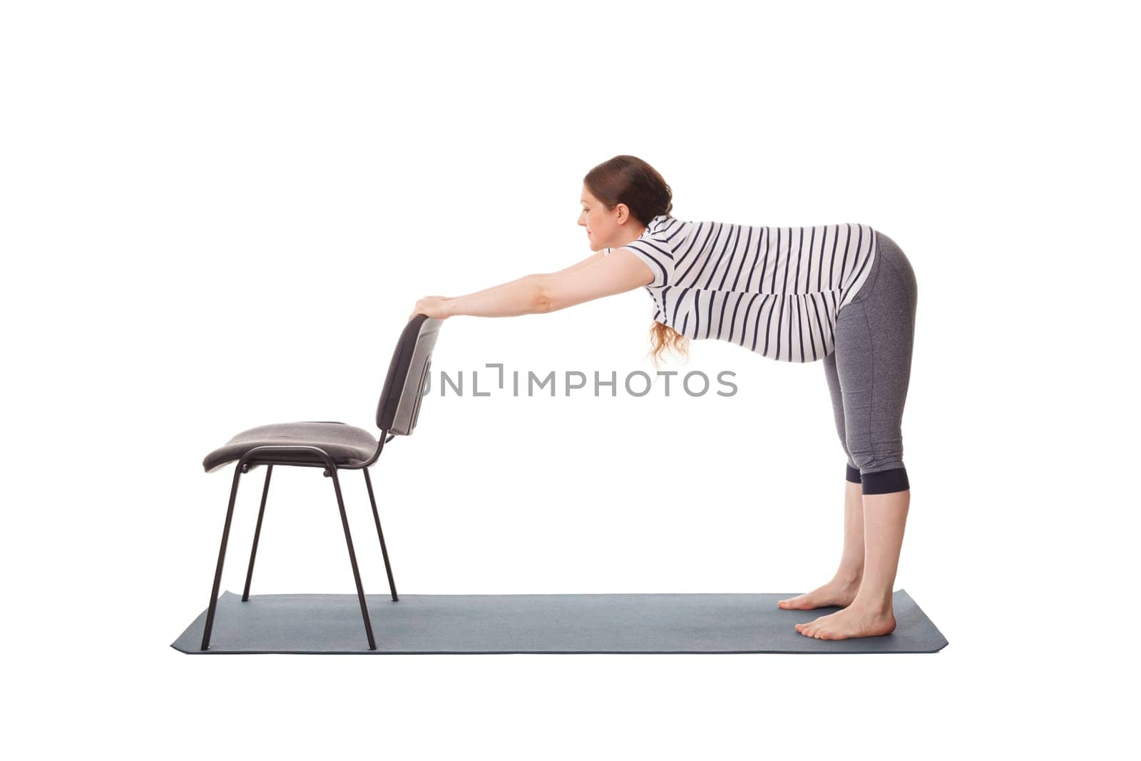 Pregnancy yoga exercise - pregnant woman doing yoga asana Uttanasana Standing Forward Fold Pose with hands on chair easy variation isolated on white background