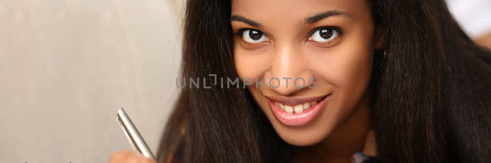 Young black woman writes in a magazine while lying on couch. Portrait of beautiful smiling woman with pen
