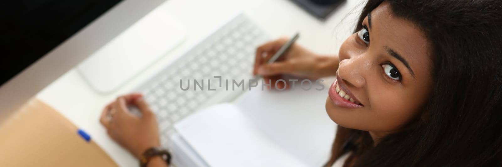 Smiling African American woman takes notes and writes in notebook. Confident business woman planning meeting work day and writing down ideas or important information