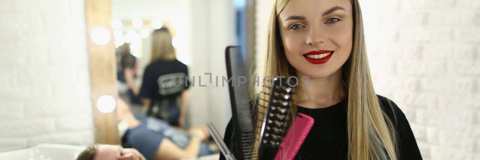 Smiling female hairdresser holding combs and scissors in barbershop by kuprevich