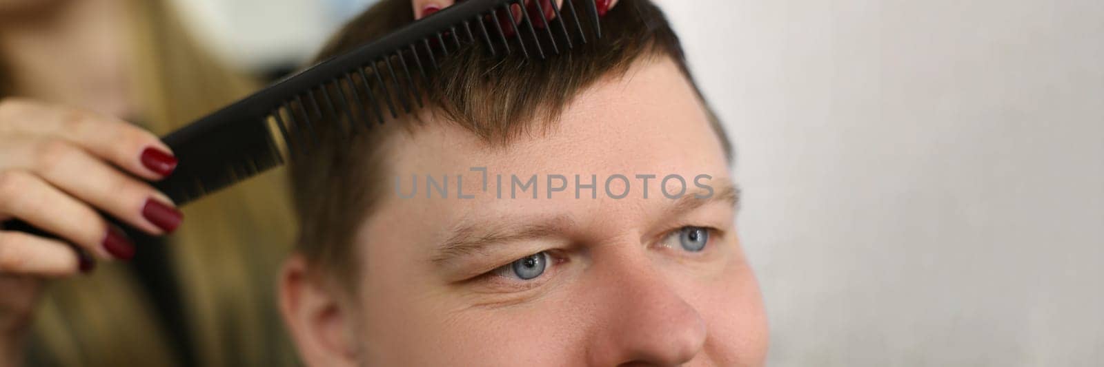 Hairdresser cuts hair with scissors and black comb. Satisfied client man sitting in barbershop salon