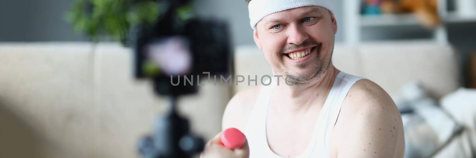 Smiling happy sports blogger blogging about exercises with dumbbells by kuprevich