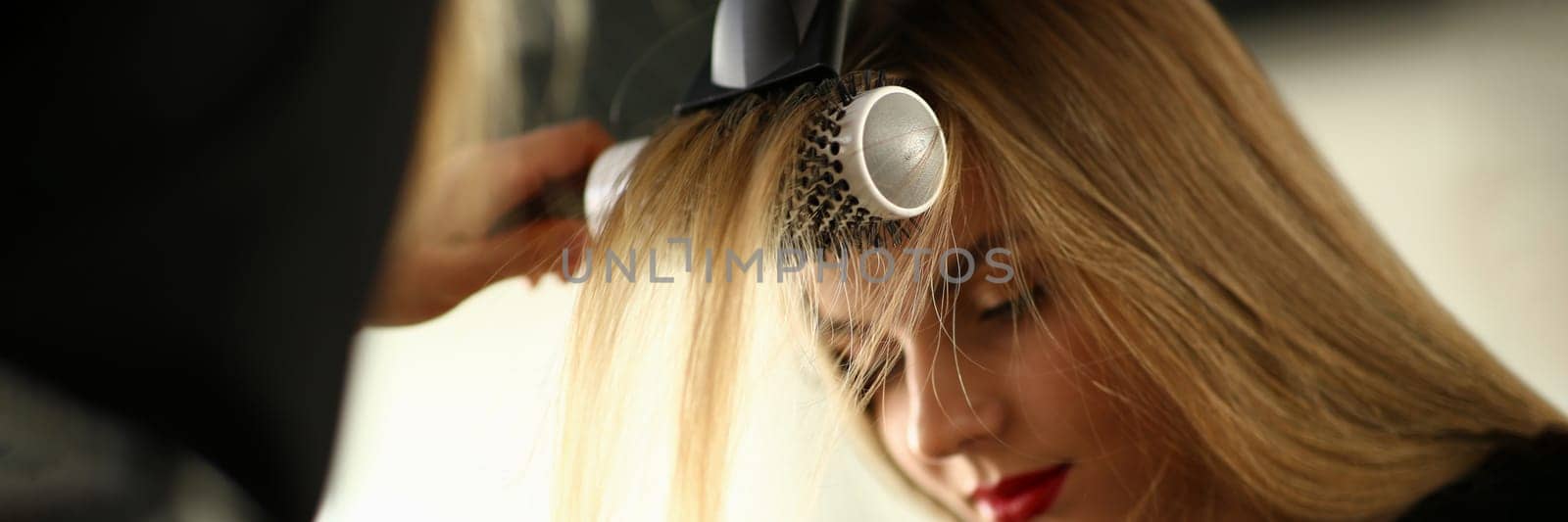 Drying blond hair with a hairdryer and a round brush in barbershop by kuprevich
