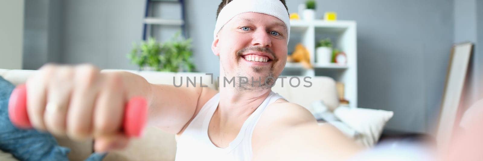 Emotional happy excited young man posing with dumbbells and taking selfie. Athlete man doing exercises with dumbbells at home