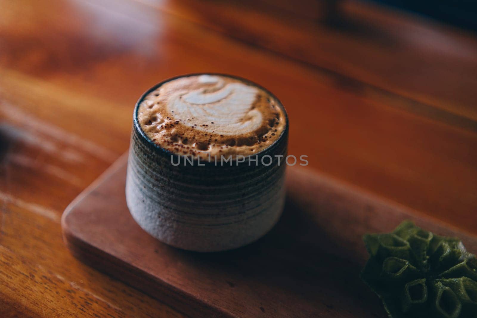 Close up shot of latte coffee cup on wood plate with brown table background. Cappuccino in ceramic mug
