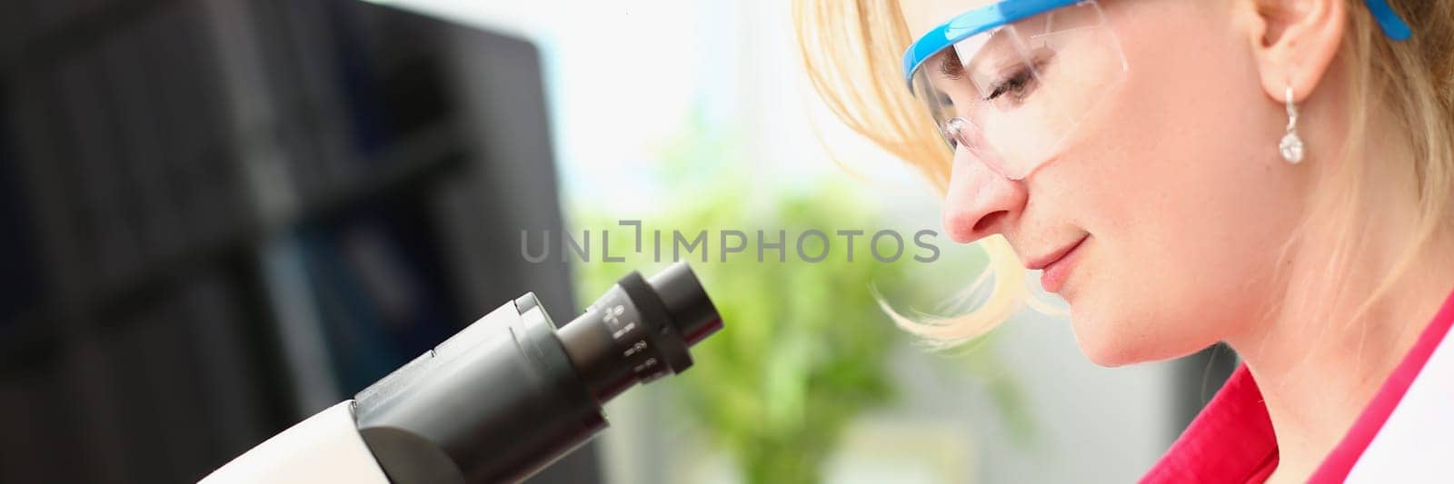 Woman scientist in glasses conducts research through microscope in chemical laboratory. Study of new bacterial viruses and toxic substances