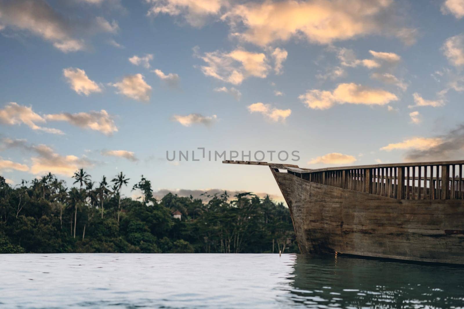 Amazing infinity pool with jungle and cloudy sky view. Wooden balcony and terrace with tropical rainforest